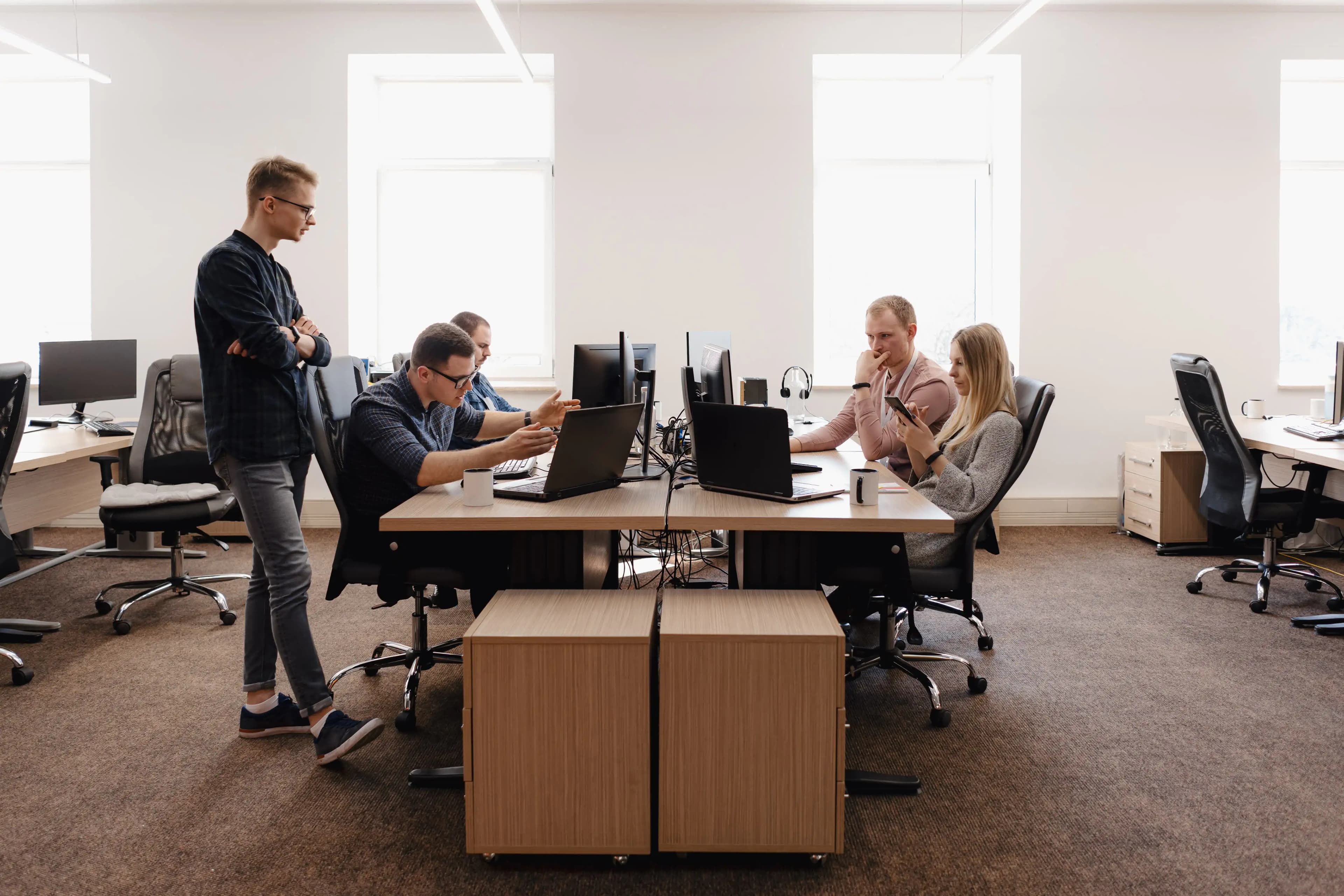 Ein Team von Menschen, die am Computer arbeiten und in einem hellen und gut organisierten Büroraum Ideen austauschen.